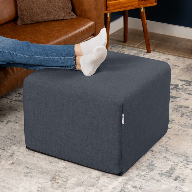 Jaxx Monroe 24in foam ottoman in denim performance fabric, used as a footrest in a living room setting