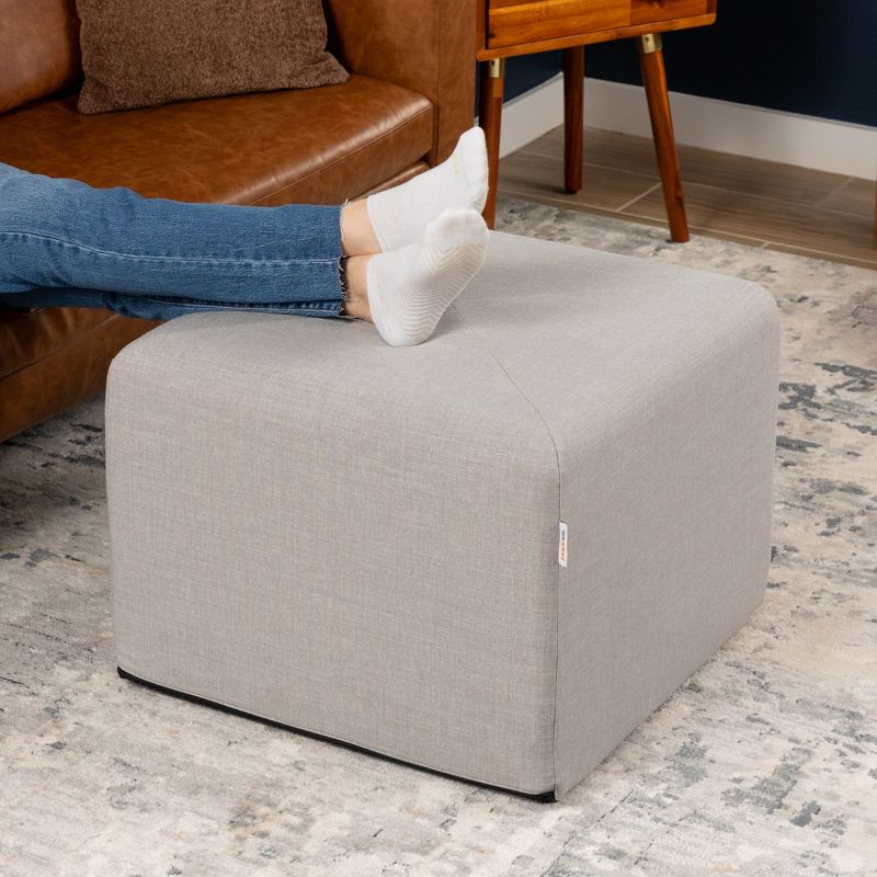 Jaxx Monroe 24in foam ottoman in grey performance fabric, used as a footrest in a living room setting