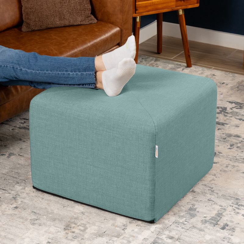 Jaxx Monroe 24in foam ottoman in lagoon performance fabric, used as a footrest in a living room setting
