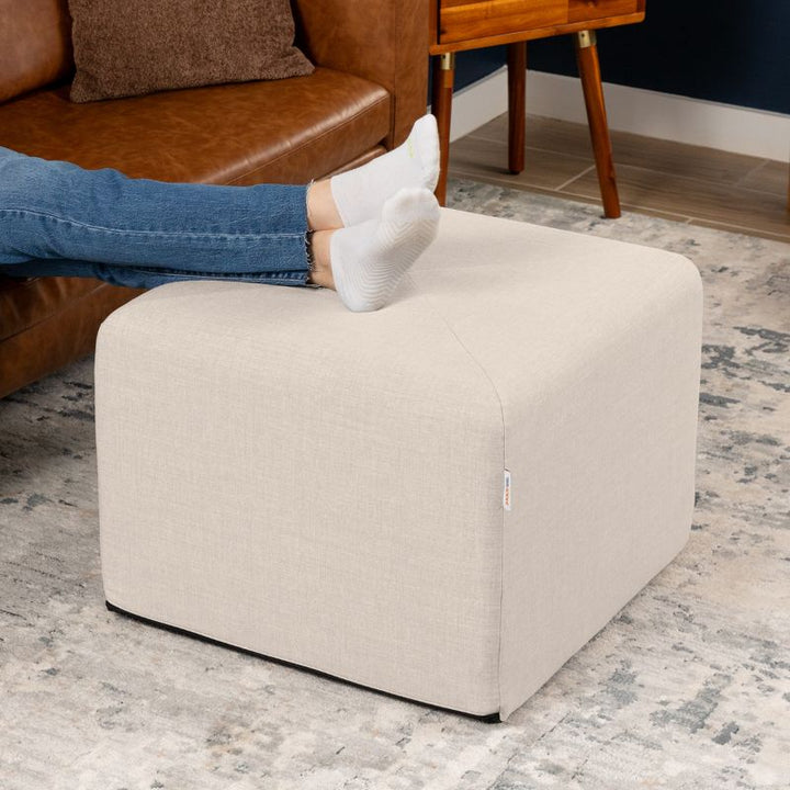 Jaxx Monroe 24in foam ottoman in mist grey performance fabric, used as a footrest in a living room setting