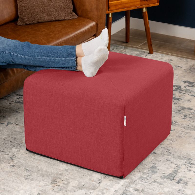Jaxx Monroe 24in foam ottoman in poppy red performance fabric, used as a footrest in a living room setting
