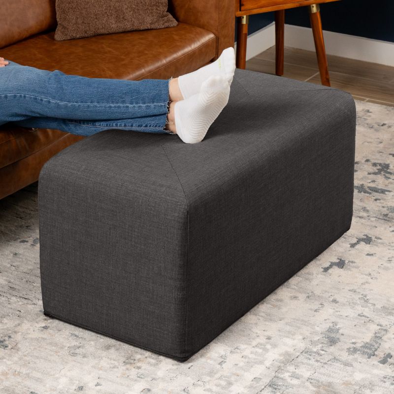 Jaxx Monroe 36in rectangular foam ottoman in charcoal performance fabric, used as a footrest in a living room setting