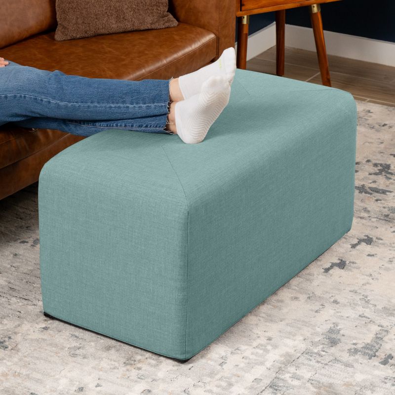 Jaxx Monroe 36in rectangular foam ottoman in lagoon performance fabric, used as a footrest in a living room setting