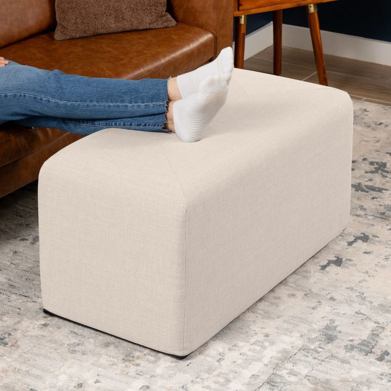 Jaxx Monroe 36in rectangular foam ottoman in mist grey performance fabric, used as a footrest in a living room setting