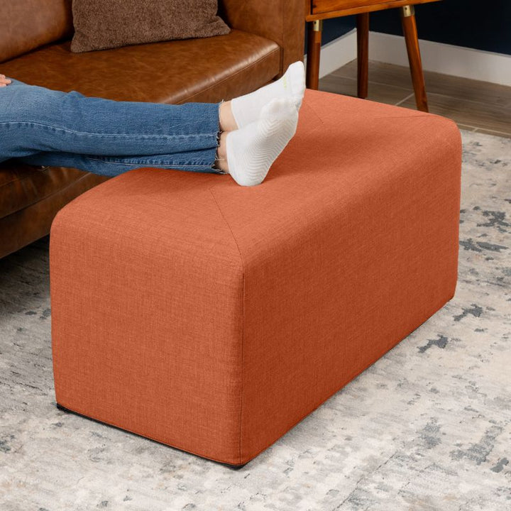 Jaxx Monroe 36in rectangular foam ottoman in canyon orange performance fabric, used as a footrest in a living room setting