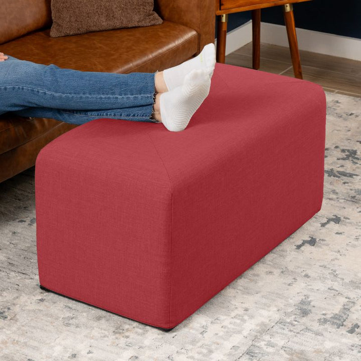 Jaxx Monroe 36in rectangular foam ottoman in poppy red performance fabric, used as a footrest in a living room setting