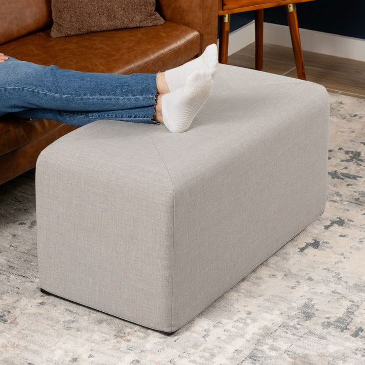 Jaxx Monroe 36in rectangular foam ottoman in shark grey performance fabric, used as a footrest in a living room setting