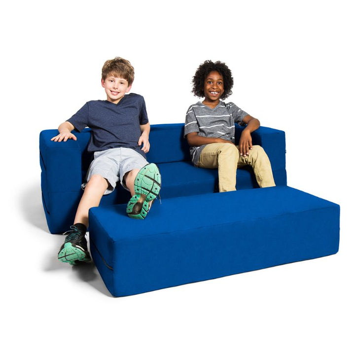 Two kids seated on the Jaxx Zipline flip sofa in blue, demonstrating the sofa and ottoman set in a home or classroom setting