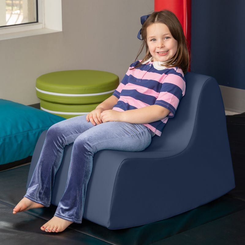 A child sitting in the navy blue Jaxx Midtown Rocker, a sensory rocking chair for kids in a classroom or therapy room
