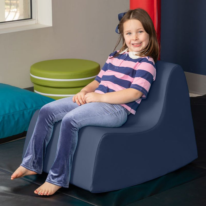 A child sitting in the navy blue Jaxx Midtown Rocker, a sensory rocking chair for kids in a classroom or therapy room