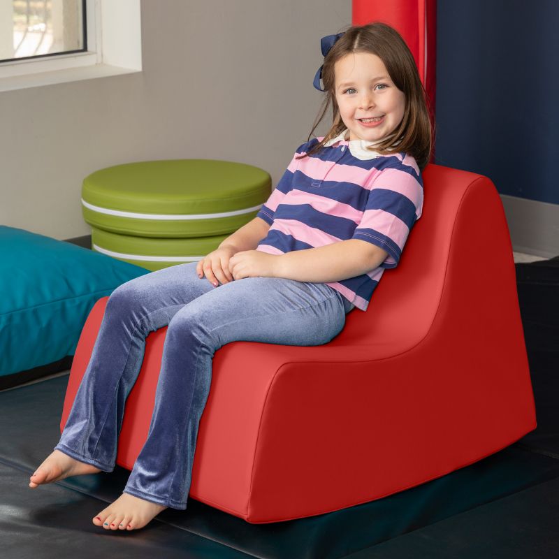 A child sitting in the red Jaxx Midtown Rocker, a sensory rocking chair for kids in a classroom or therapy room