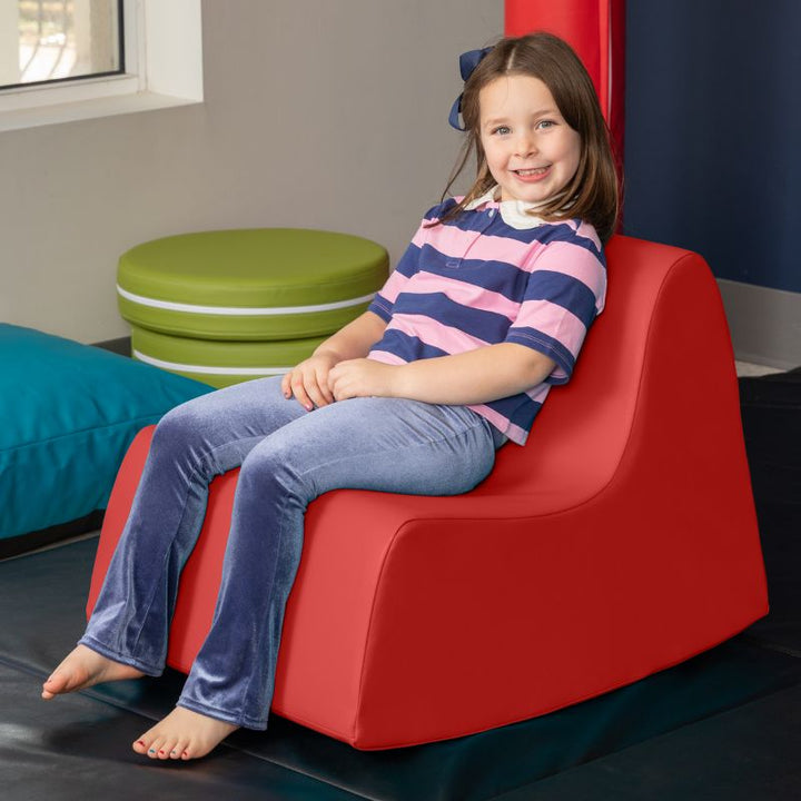 A child sitting in the red Jaxx Midtown Rocker, a sensory rocking chair for kids in a classroom or therapy room