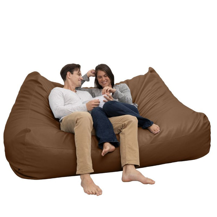 Two people relaxing on the Jaxx Lozia faux leather loveseat in walnut, easy-clean soft seating for reception areas
