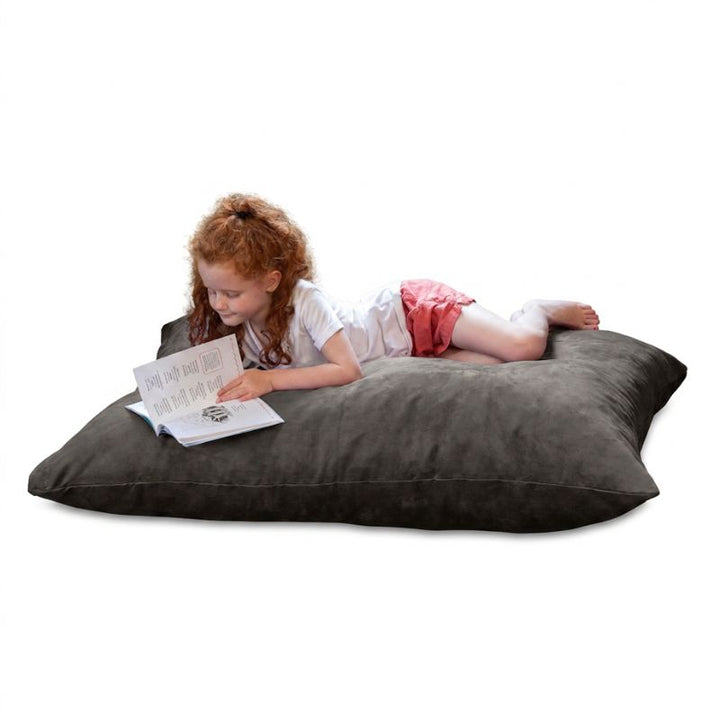 Child reading a book on a Jaxx Pillow Saxx 4 bean bag floor pillow in Black microsuede, a cozy kids floor pillow for reading nooks