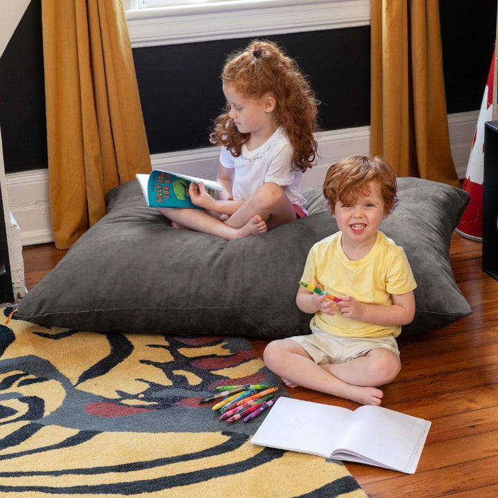 Girl reading and a younger child colouring beside a Charcoal Jaxx Pillow Saxx 4 kids floor pillow, soft bean bag floor seating for shared play