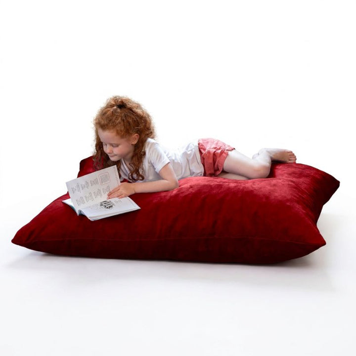 Child relaxing with a book on a Jaxx Pillow Saxx 4 bean bag floor pillow in Cherry microsuede, a bright kids floor pillow for reading nooks