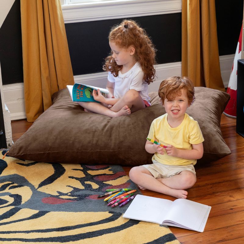 Two kids reading and colouring on and beside a Chocolate Jaxx Pillow Saxx 4 kids floor pillow in a cozy bedroom corner
