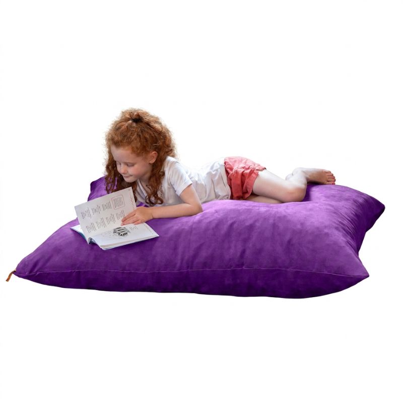 Girl stretched out with a book on a Grape microsuede Jaxx Pillow Saxx 4 kids floor pillow, soft bean bag seating for calm corners