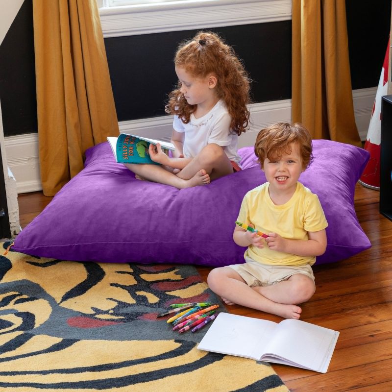 Girl reading on a Grape Jaxx Pillow Saxx 4 kids floor pillow while a younger child colours nearby, a shared bean bag floor cushion for calm corners