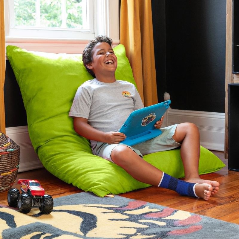 Boy relaxing against a Lime Jaxx Pillow Saxx 4 bean bag floor pillow, a cheerful kids floor cushion set upright in a playroom