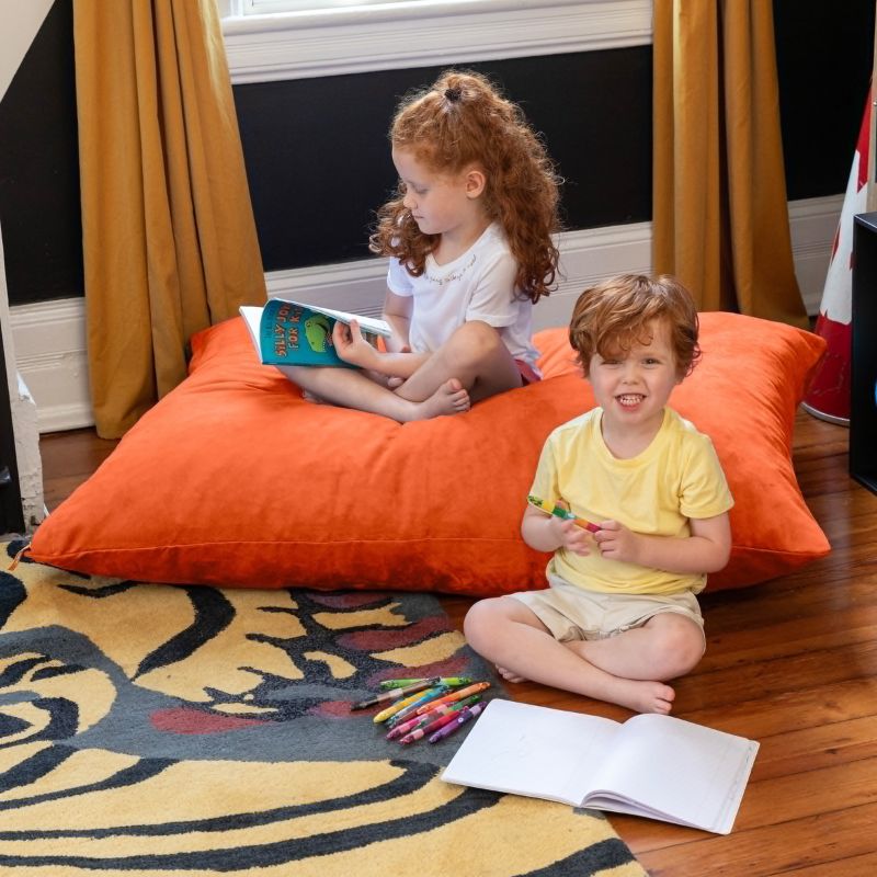 Two children reading and colouring together on a Mandarin Jaxx Pillow Saxx 4 kids floor pillow, a vibrant reading nook floor cushion