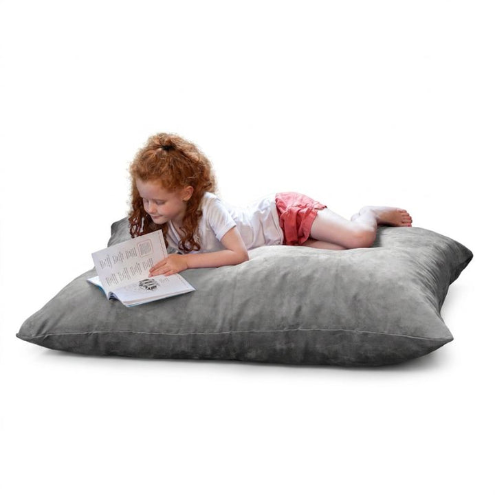 Child reading a book on a Jaxx Pillow Saxx 4 bean bag floor pillow in Platinum microsuede, a soft neutral kids floor pillow for classrooms and homes