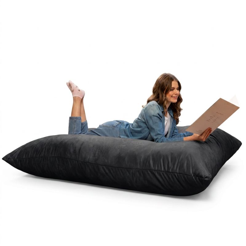 Woman reading while stretched out on a Jaxx Pillow Saxx 5 giant bean bag floor pillow in Black, an oversized floor cushion for lounging
