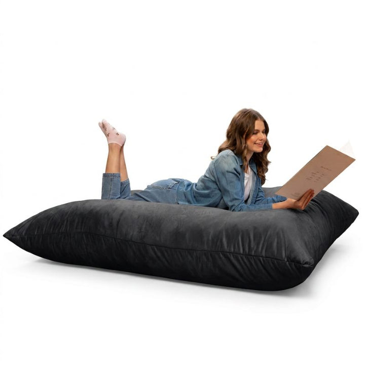 Woman reading while stretched out on a Jaxx Pillow Saxx 5 giant bean bag floor pillow in Black, an oversized floor cushion for lounging
