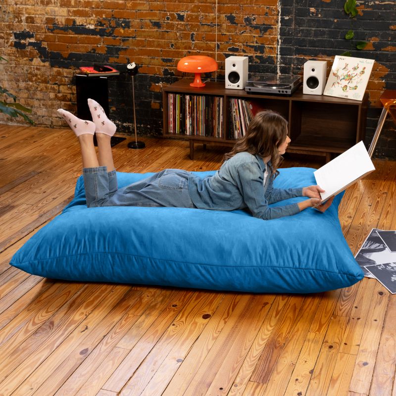 Woman reading on a Blueberry Jaxx Pillow Saxx 5 bean bag floor pillow, an oversized floor cushion in a relaxed loft-style space
