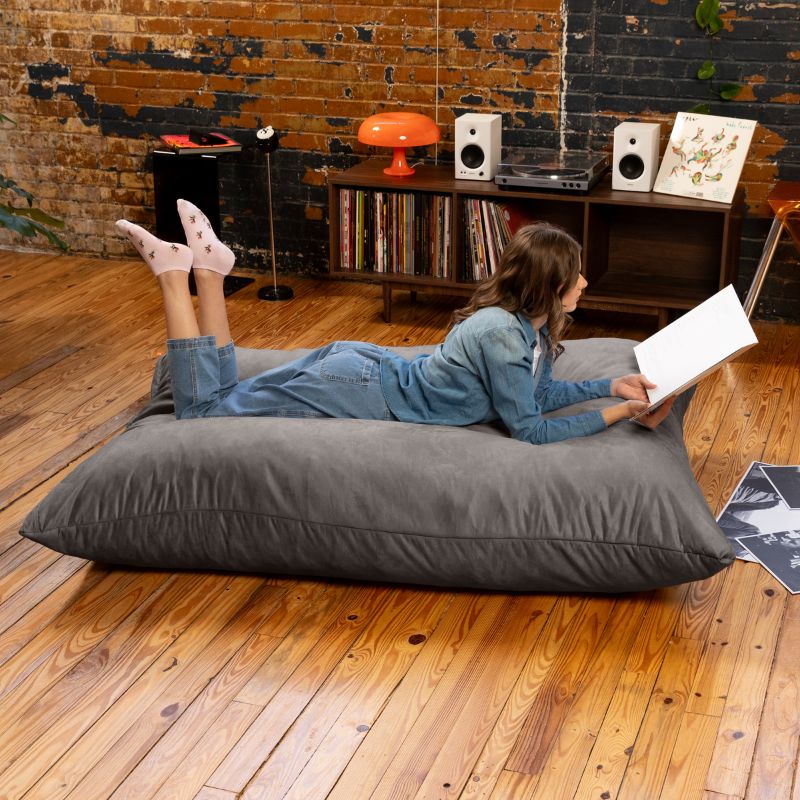 Reader lying on a Charcoal Jaxx Pillow Saxx 5 bean bag floor pillow on a hardwood floor, a giant floor cushion for rec rooms