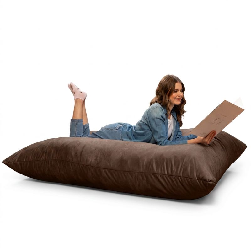 Woman enjoying a book on a Jaxx Pillow Saxx 5 giant bean bag floor pillow in Chocolate, a soft oversized crash pillow
