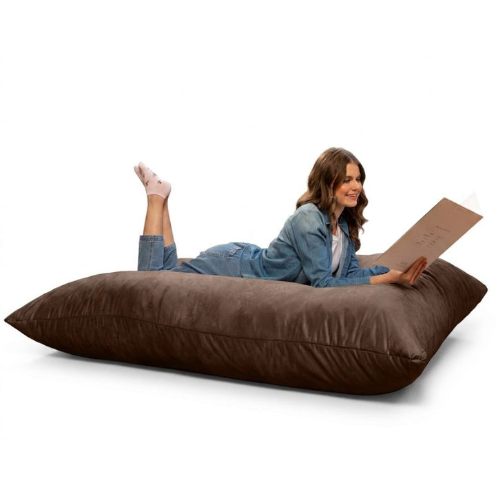 Woman enjoying a book on a Jaxx Pillow Saxx 5 giant bean bag floor pillow in Chocolate, a soft oversized crash pillow