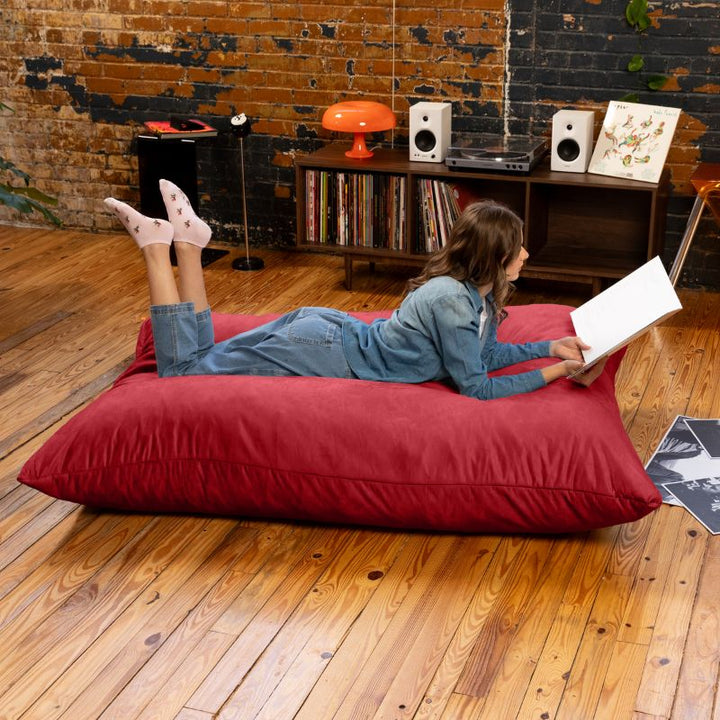 Adult reading a record sleeve on a Cinnabar Jaxx Pillow Saxx 5 bean bag floor pillow, a bold giant crash pillow for living spaces