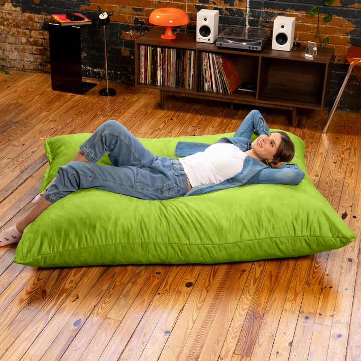 Woman lounging on a Jaxx Pillow Saxx 5 giant bean bag floor pillow in Lime, a bright oversized floor cushion for downtime at home