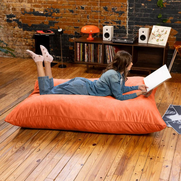 Reader stretched out on a Mandarin Jaxx Pillow Saxx 5 bean bag floor pillow, a vibrant giant floor cushion for calm corners