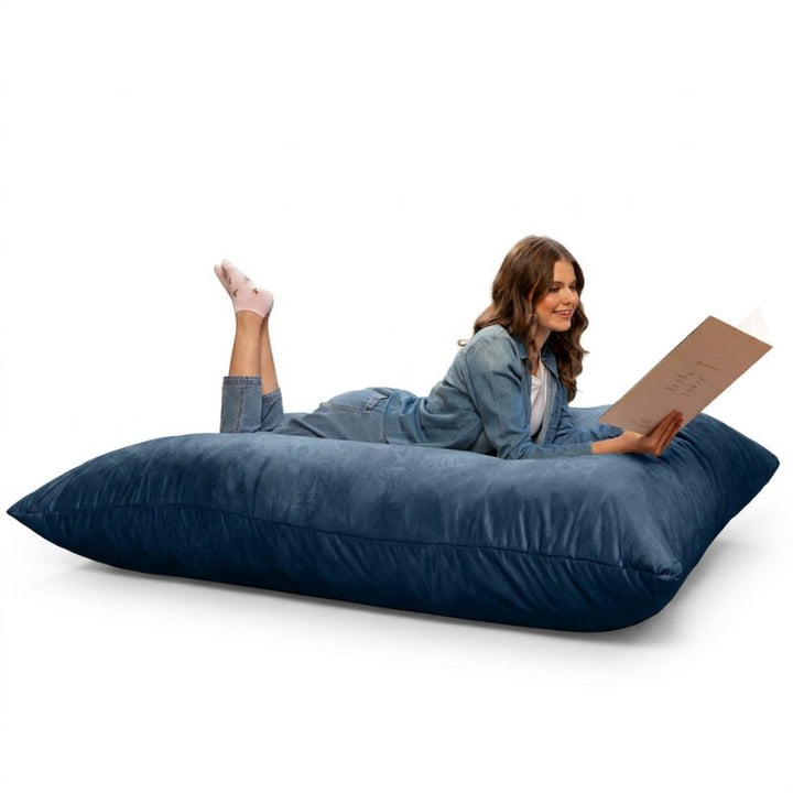 Woman reading on a Jaxx Pillow Saxx 5 giant bean bag floor pillow in Navy, a deep-toned oversized floor cushion for lounging
