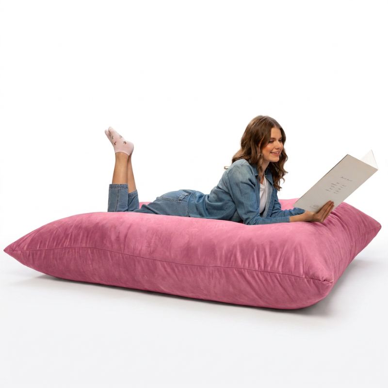 Adult stretched out with a book on a Pink Jaxx Pillow Saxx 5 bean bag floor pillow, a soft giant floor cushion for calm corners