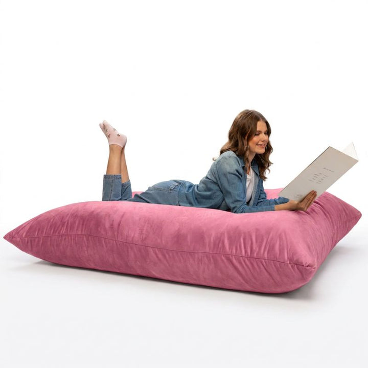 Adult stretched out with a book on a Pink Jaxx Pillow Saxx 5 bean bag floor pillow, a soft giant floor cushion for calm corners