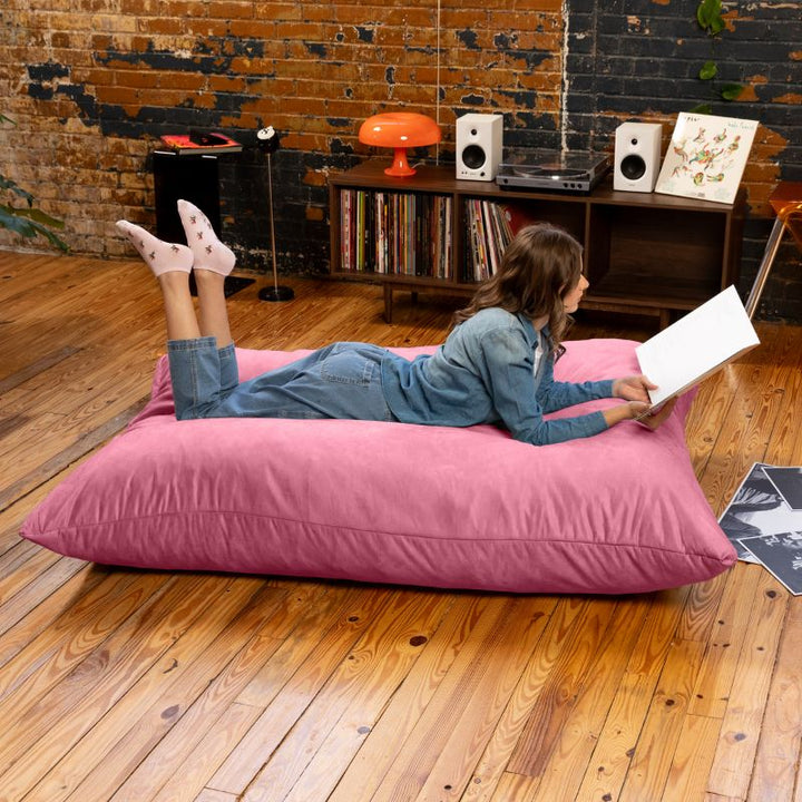 Woman reading on a Pink Jaxx Pillow Saxx 5 bean bag floor pillow, a soft oversized floor cushion for sensory rooms and family spaces