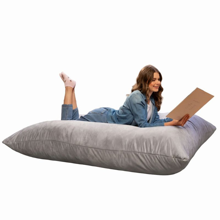 Woman lying on a Jaxx Pillow Saxx 5 giant bean bag floor pillow in Platinum, a light neutral crash pillow for homes and classrooms