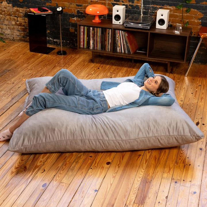 Woman lying back on a Jaxx Pillow Saxx 5 giant bean bag floor pillow in Platinum, a light neutral floor cushion for homes and classrooms