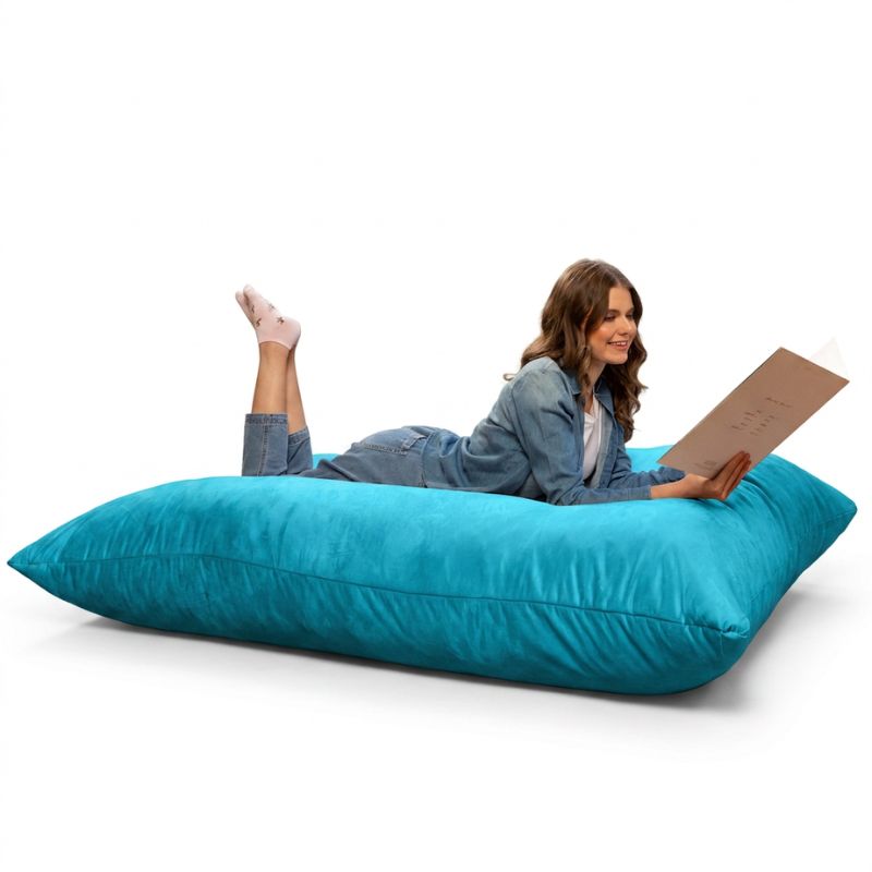 Reader relaxing on a Teal Jaxx Pillow Saxx 5 bean bag floor pillow, a vibrant giant floor cushion for sensory rooms and family spaces