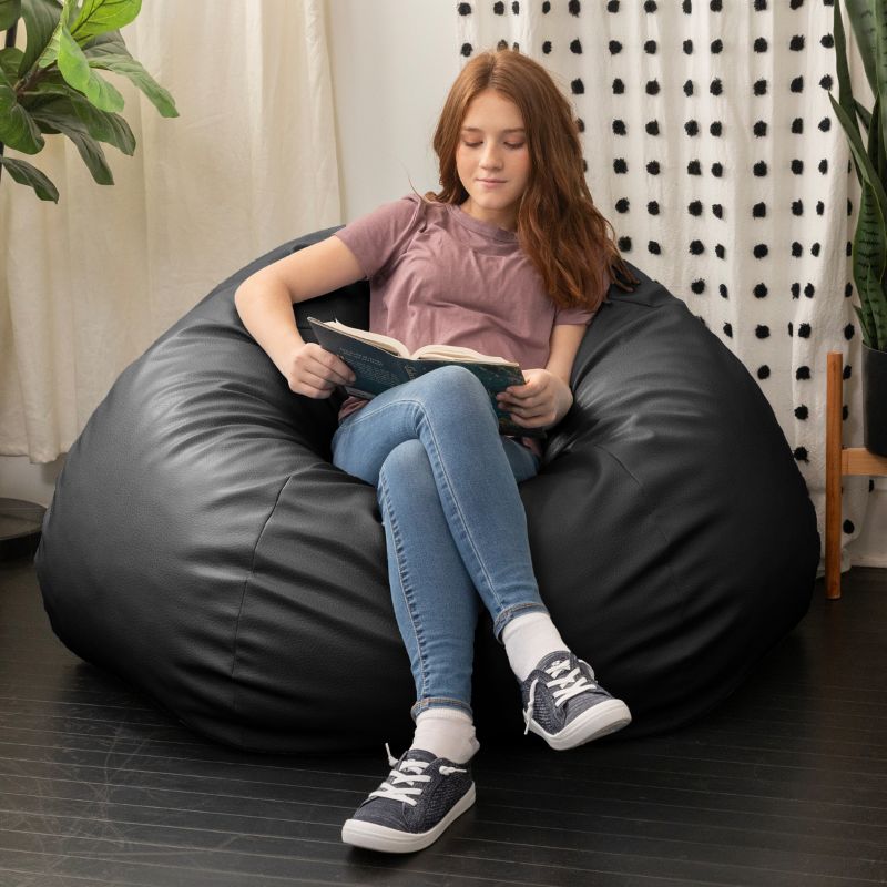 Child reading a book in the Jaxx Pazi faux leather bean bag pod chair in Black in a cozy reading nook