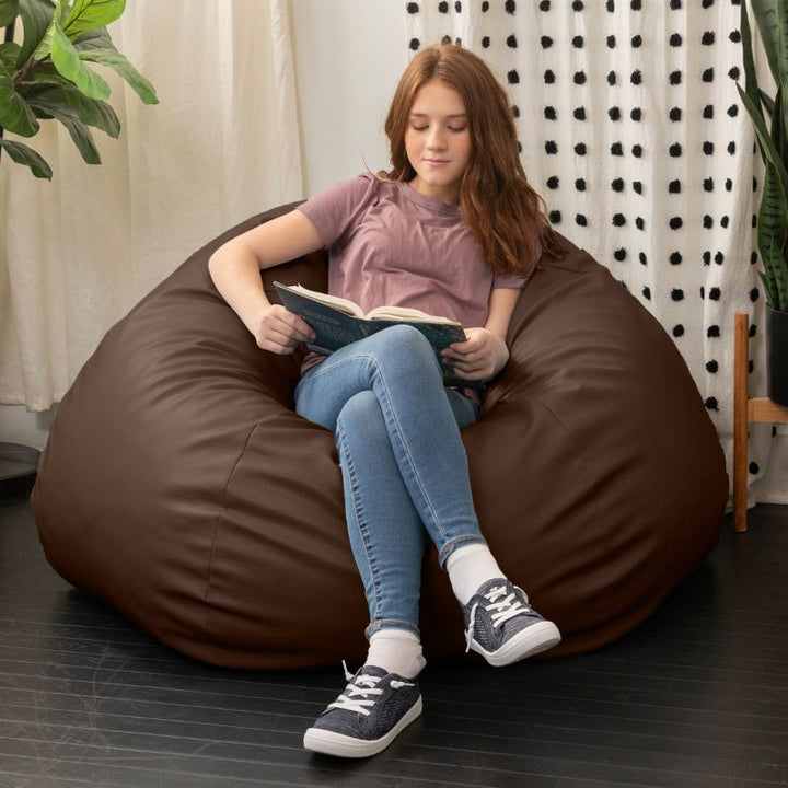 Child reading a book in the Jaxx Pazi faux leather bean bag pod chair in Chocolate in a cozy reading nook