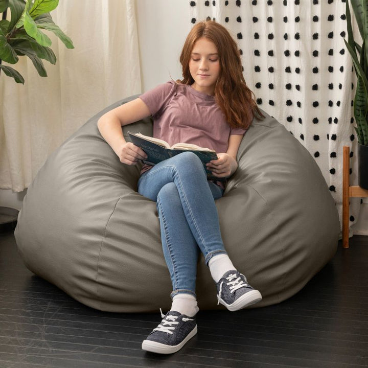 Child reading a book in the Jaxx Pazi faux leather bean bag pod chair in Gun Metal in a cozy reading nook