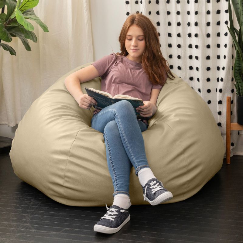 Child reading a book in the Jaxx Pazi faux leather bean bag pod chair in Natural Beige in a cozy reading nook