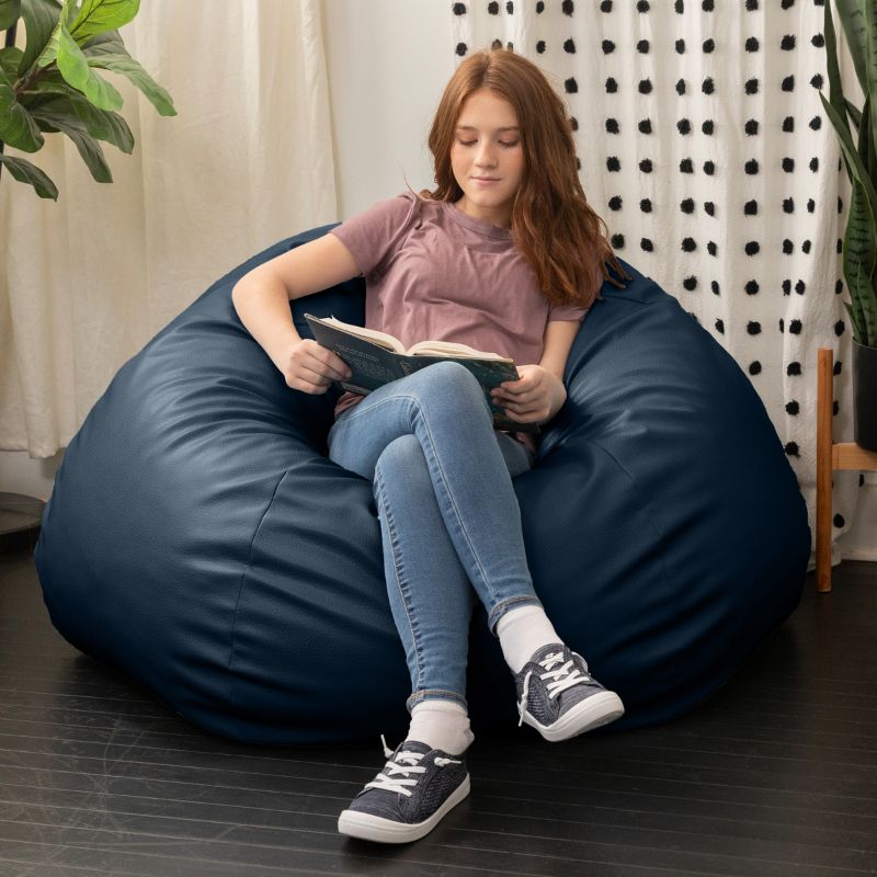 Child reading a book in the Jaxx Pazi faux leather bean bag pod chair in Oxford Blue in a cozy reading nook
