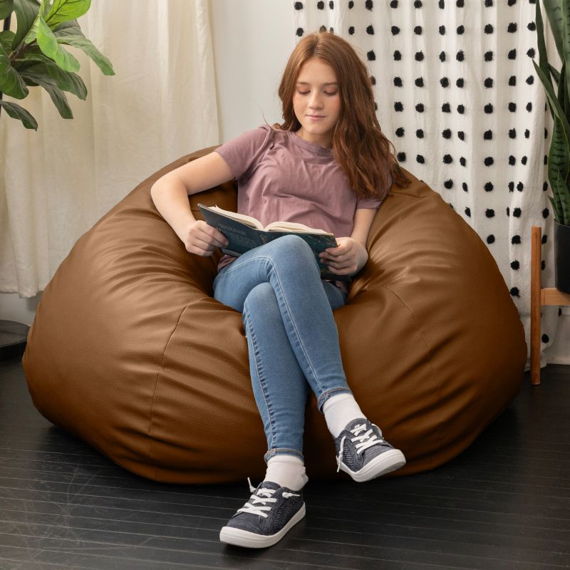Child reading a book in the Jaxx Pazi faux leather bean bag pod chair in Walnut in a cozy reading nook