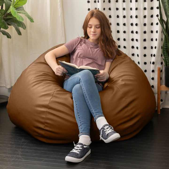 Child reading a book in the Jaxx Pazi faux leather bean bag pod chair in Walnut in a cozy reading nook