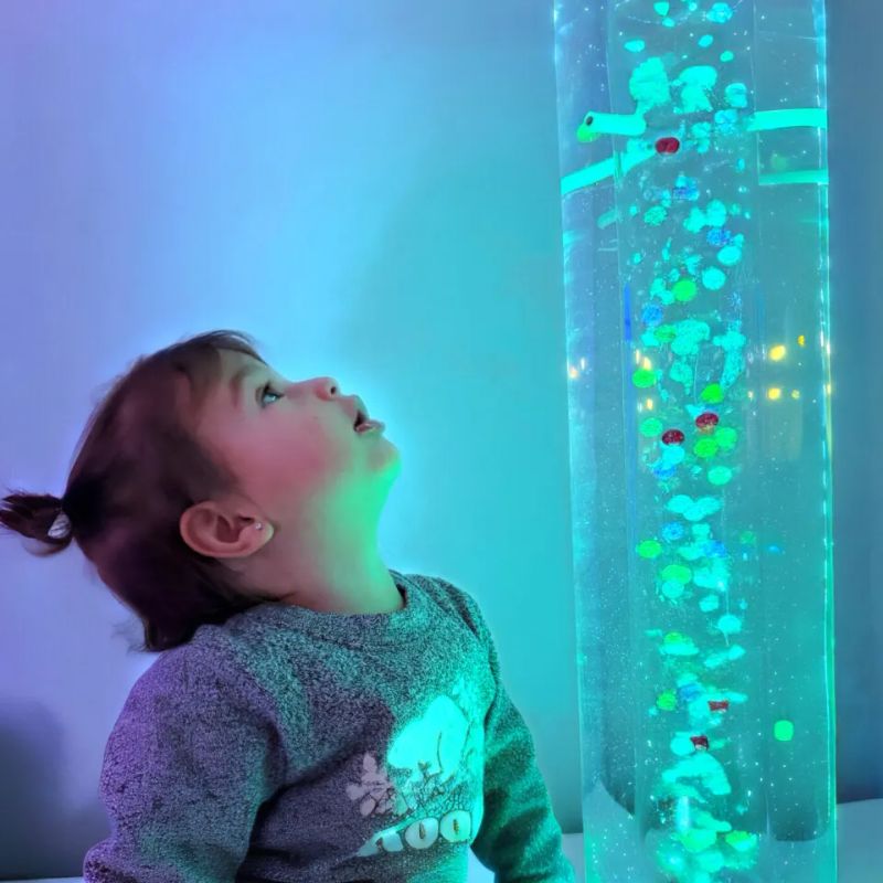 Toddler looking up in wonder at the TFH Standard Bubble Tube Insert with cascading balls and beads, a 6 inch diameter sensory bubble tube insert for visual tracking and calm